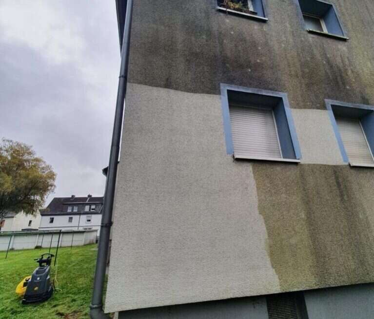 Graues Mehrfamilienhaus mit verschmutzter Fassade vor der Reinigung