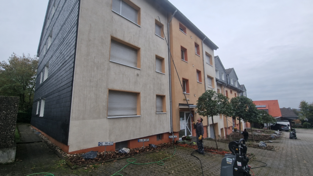 Ein Arbeiter reinigt mit Teleskopstange die Dachrinne eines Mehrfamilienhauses