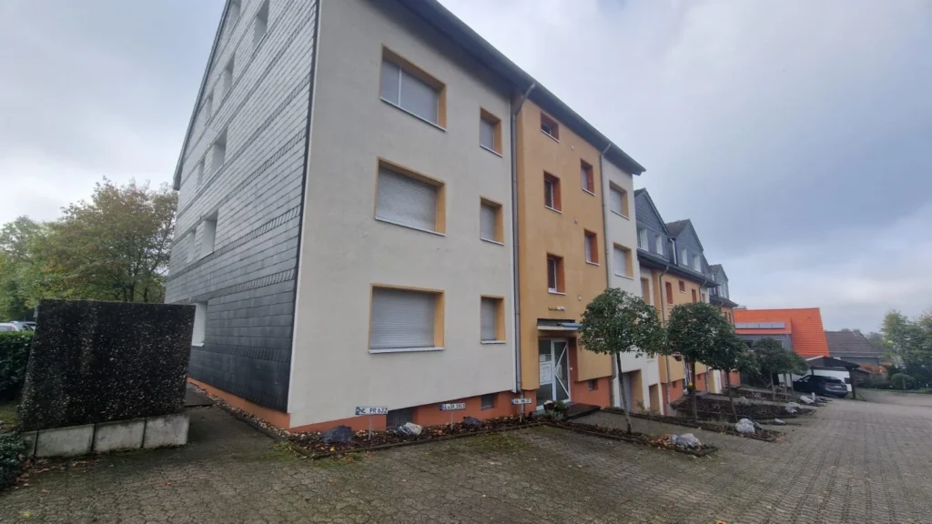 Mehrfamilienhaus mit weißer Fassade, grauer Schieferwand und orangem Eingangsbereich